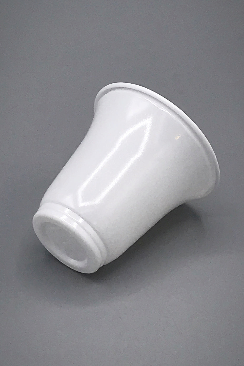 A glossy white polystyrene single serve recyclable cup with a flared rim, shown from a side angle on a neutral grey background.