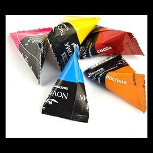 Five individually wrapped cone-shaped candy pieces from the brand Novaroma, arranged in a fan shape on a plain white background. The wrappers feature different colours: pink, yellow, red, blue, and orange, with black and white branding.